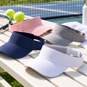 Adjustable sun visors in white, navy, pink and gray displayed beside a tennis court.